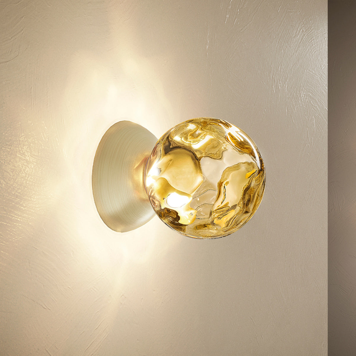 Murané Glass Sphere Wall & Ceiling Light 15cm in Brushed Champagne, with a dimpled amber glass globe on a dome mount, illuminated against a plain wall.