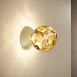 Murané Glass Sphere Wall & Ceiling Light 15cm in Brushed Champagne, with a dimpled amber glass globe on a dome mount, illuminated against a plain wall.