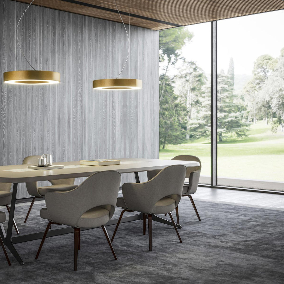 Two Silver Ring gold-finish LED ring pendant lights hang above a dining table in a modern dining room with grey wood-panelled walls and floor-to-ceiling windows.