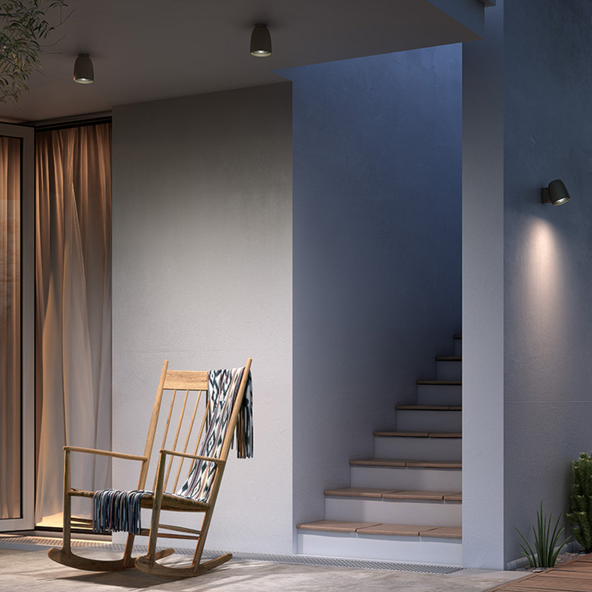 Nut PF/10 small bell-shaped outdoor ceiling light in black, mounted on a grey wall above a staircase in an outdoor seating area with a wooden rocking chair.