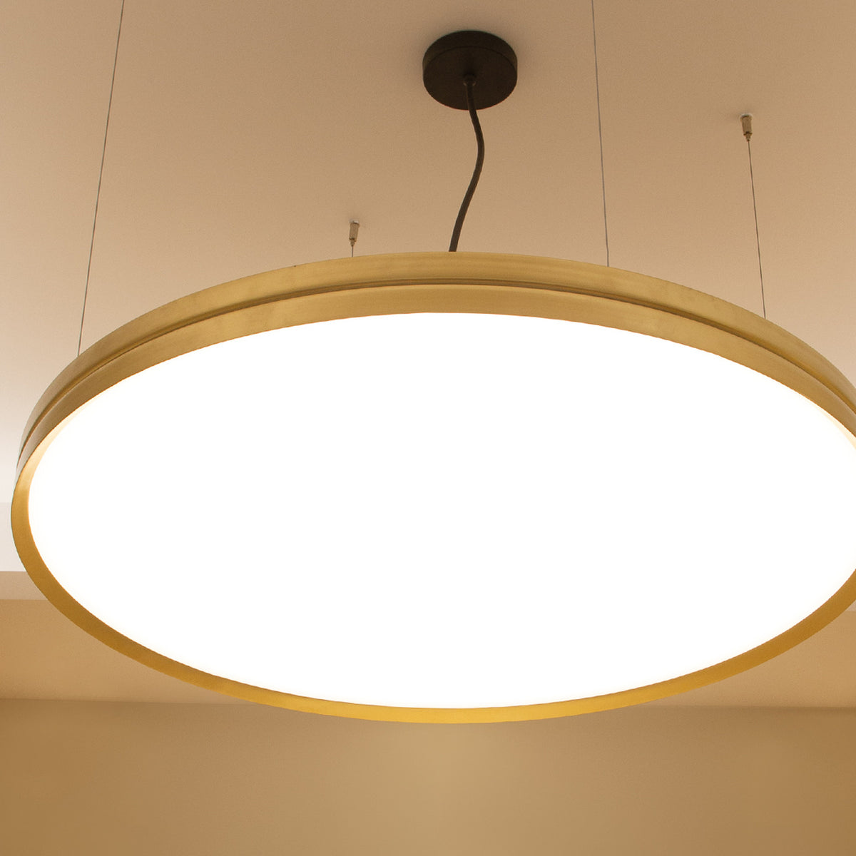 Lite Hole S90 round LED pendant light with a brushed gold aluminium frame and flat illuminated white disc, suspended from a ceiling mount by thin cables.