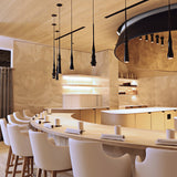 Slend 02 Aluminium Pendant Light in black, shown as multiple slim tapering fixtures hanging above a curved dining bar in a restaurant setting.