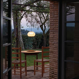 Garota S/02 Globe LED Outdoor Pendant Light in Ivory White, woven globe shade illuminated above an outdoor dining table on a covered garden patio at dusk.