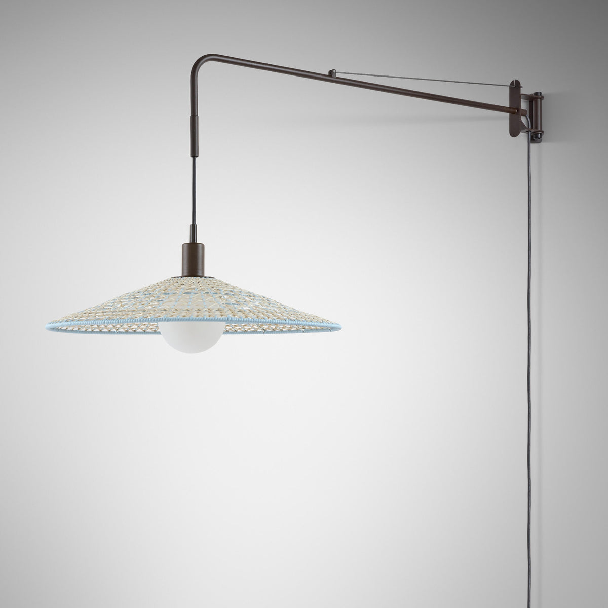 Nans 55 A/98 plug-in wall light with a long swing arm in brown finish and a wide woven cone shade in beige with light blue detailing, shown against a plain light background.