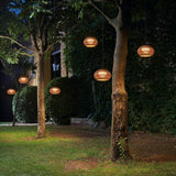Garota Hang Globe LED outdoor pendant lights with brown woven globe shades hung from trees, glowing warmly in a garden setting at night.