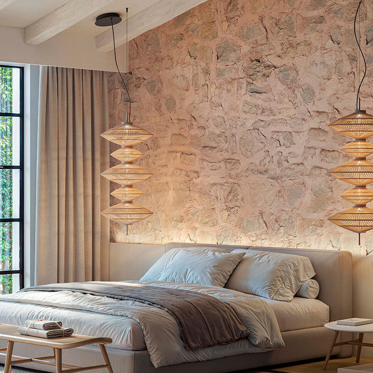Yuyun S/5C fabric LED pendant light with five stacked woven shades in satin beige, shown in pairs above a bed in a stone-walled bedroom.
