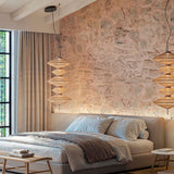 Yuyun S/5C fabric LED pendant light with five stacked woven shades in satin beige, shown in pairs above a bed in a stone-walled bedroom.