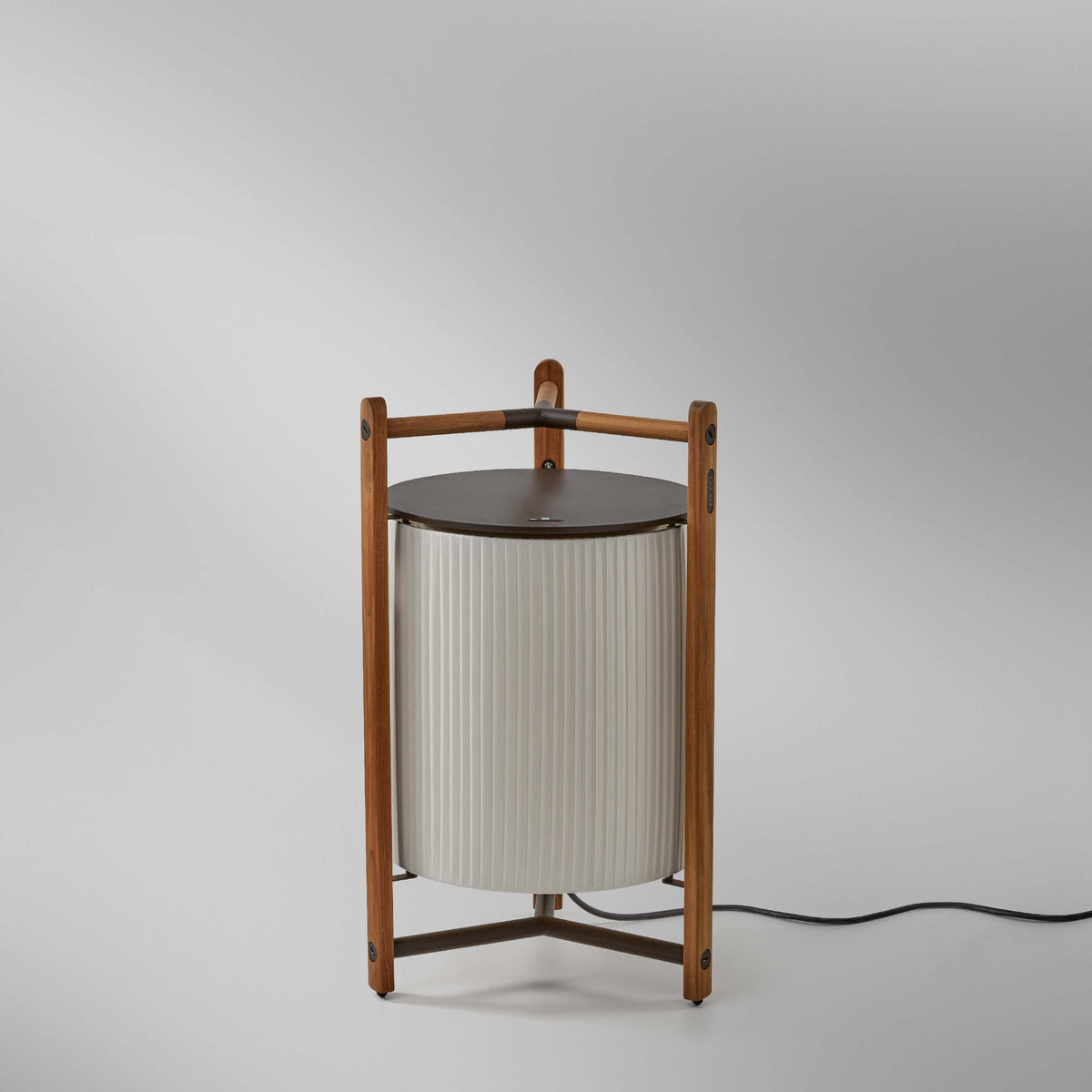Kando P/76 Ribbon LED floor lamp with a pleated white translucent cylindrical shade, dark cap, and teak wood frame with tripod base, on a plain light background.