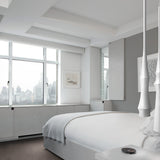 Slend 01 Aluminium Pendant Light in white, slim tapering form, shown in pairs above a bed in a modern bedroom with city views.