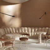 Opuntia 130 Aluminium LED Wall Lights in matte black with slim long-reach arms and dome heads, mounted on a curved brown wall above a beige banquette seating area.