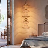 Yuyun S/9C LED pendant light with nine stacked woven cotton shades in satin beige, hung beside a bed in a bedroom with rattan headboard and bedside table.