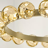 Close-up of the Murané R 25 ring chandelier showing a brushed champagne band set with textured caramel glass spheres, lit from within against a plain light background.