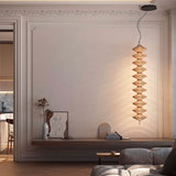 Yuyun S/11S fabric LED pendant light in satin beige, eleven stacked woven cotton tiers on a slim stem, shown hanging in a living room above a wooden console.