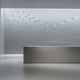 Bella Direct LED pendant lights in Brushed Bronze, multiple slim disc heads on thin stems suspended in a wave arrangement above a reception desk in a modern interior.