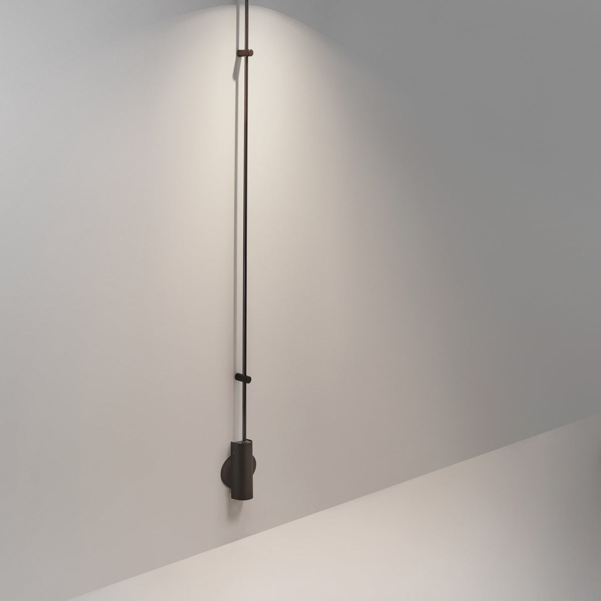Platet A/06 aluminium LED wall light in matte black, a tall slim rod with a small cylindrical shade mounted low on a plain grey wall.