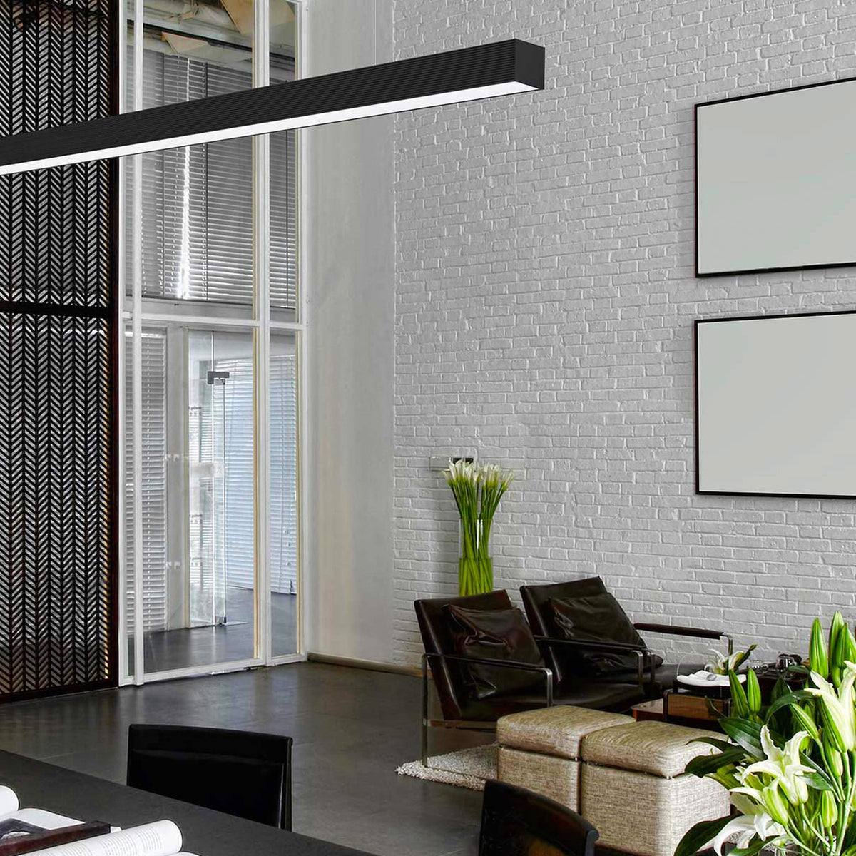 Brooklyn Line Aluminium Linear LED Pendant Light 152cm, black slim bar fixture, hung in a living space with brick wall, armchairs, and framed art.