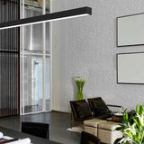 Brooklyn Line Aluminium Linear LED Pendant Light 152cm, black slim bar fixture, hung in a living space with brick wall, armchairs, and framed art.