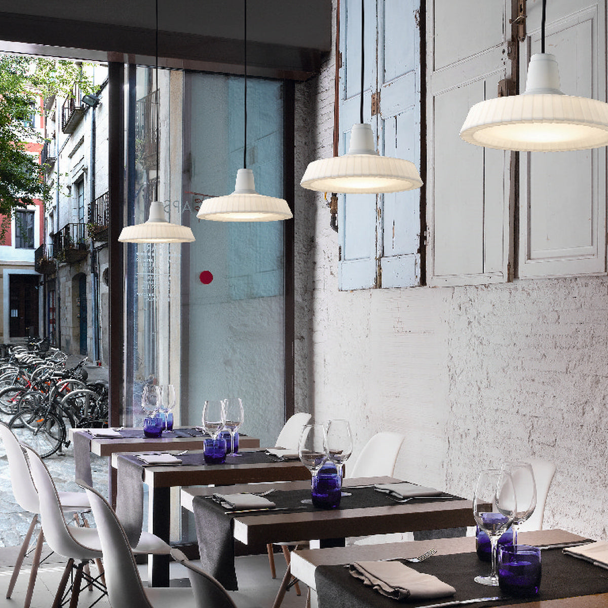 Marietta S/32 dome LED pendant lights with pleated white shades and black cables, hung above restaurant tables near a bright window.