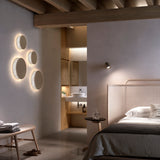Helios A/01 round LED wall lights in Oak Brown & Beige fabric, five discs with warm halo glow, mounted beside a bedroom doorway.
