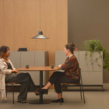 Speers SR L pendant light in matte black with a wide, shallow cone shade, hung on a slim cable above a wooden dining table in a living room setting.