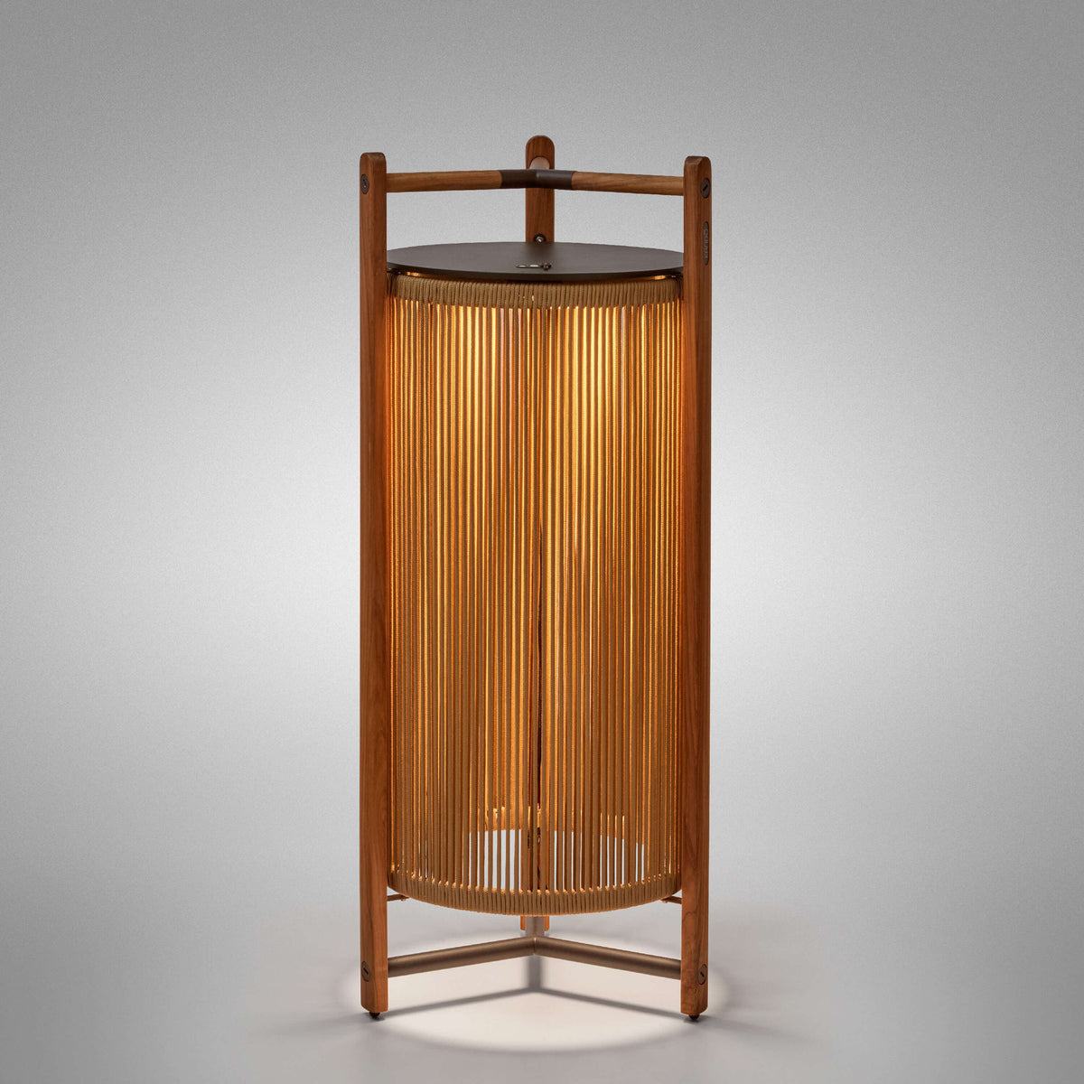 Kando P/111/R rechargeable outdoor floor lamp with teak wood frame, sand nautical cord cylinder, brown top disc and three-legged base, lit from within on a plain light background.