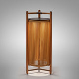 Kando P/111/R rechargeable outdoor floor lamp with teak wood frame, sand nautical cord cylinder, brown top disc and three-legged base, lit from within on a plain light background.
