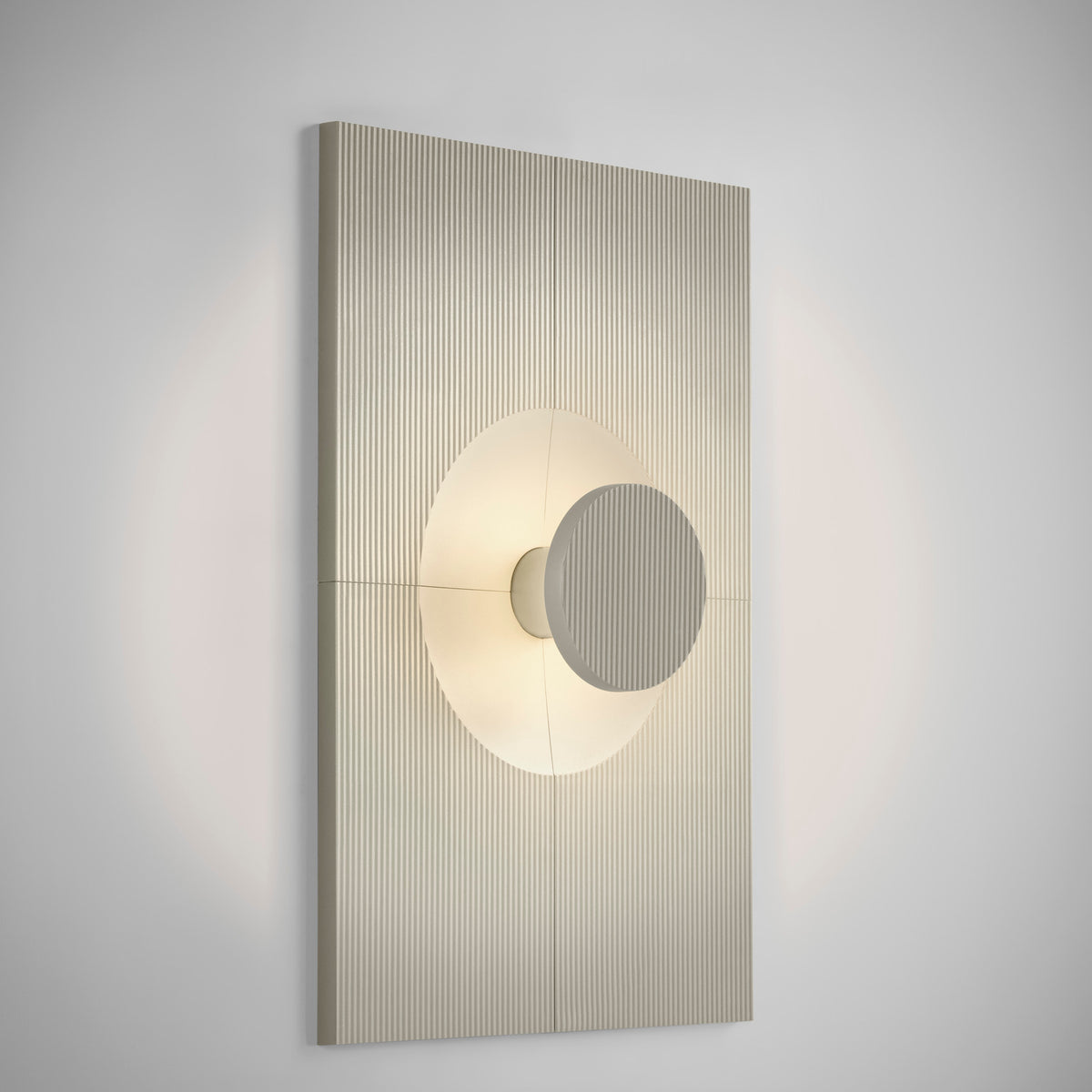 Arid Wall Light Tile in Textured Pebble Grey, a vertically fluted aluminium panel with a smooth curved centre framing a lit circular cutout, shown on a plain light background.