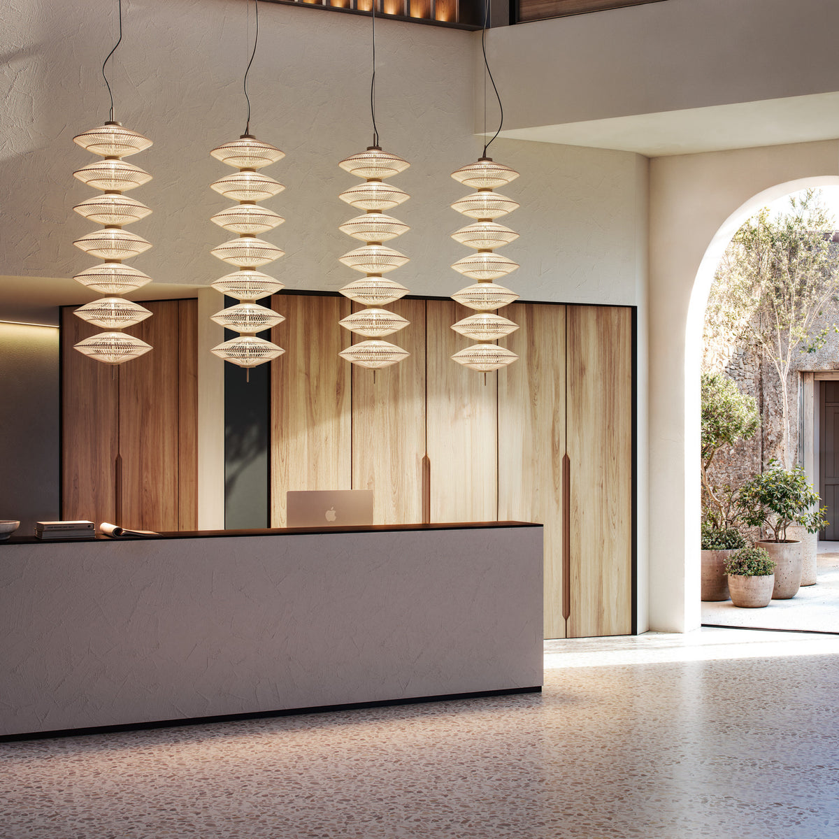 Yuyun S/7L Fabric LED Pendant Light in Satin Beige, four tiered woven cotton fixtures with seven stacked tiers each, shown above a wood-panelled reception desk.