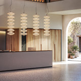 Yuyun S/7L Fabric LED Pendant Light in Satin Beige, four tiered woven cotton fixtures with seven stacked tiers each, shown above a wood-panelled reception desk.