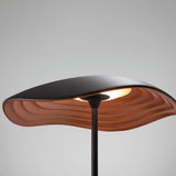 Valentina M/29 table lamp with a wavy leaf-shaped shade, black on top and ribbed copper underneath, on a slim black stem, shown close-up against a plain grey background.