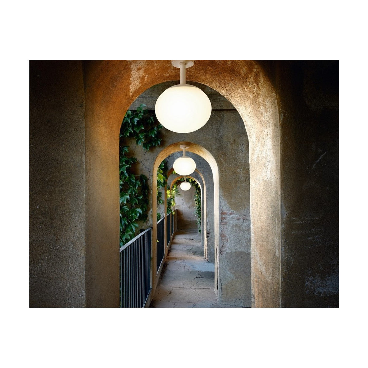 Elipse PF/30 Globe LED Outdoor Ceiling Light in white, illuminated in a vaulted stone archway corridor, shown with multiple fixtures receding along the covered walkway.
