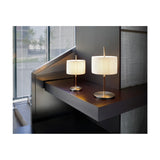 Two Danona Mini table lamps with pleated white ribbon drum shades on slim satin nickel stems and round bases, shown on a dark wood shelf in a modern interior.