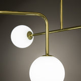 Close-up of the Lumorne 4 Light Glass Globe Chandelier in polished brass, showing angular metal arms and two opal glass globes at varying heights.