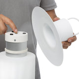 Nautic LED Rechargeable Outdoor Table Lamp in white being assembled, showing the detachable cap with control buttons, wide flat brim and cylindrical diffuser base, held against a plain background.