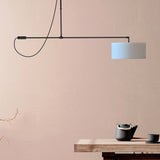 Raisa Fabric Drum Pendant Light in matt black, with a slim offset arm holding a white fabric drum shade, shown above a dining table in a pink-toned room.