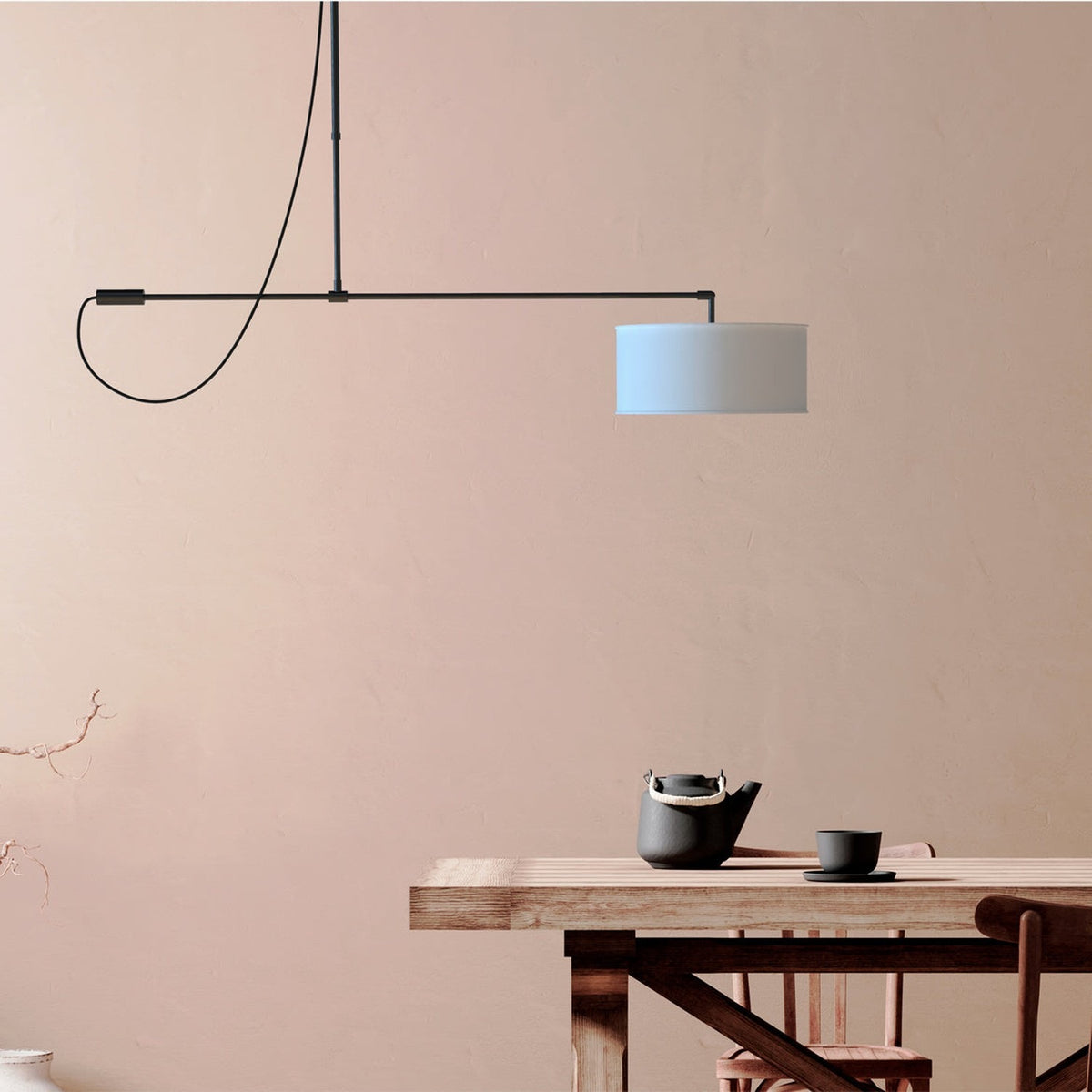 Raisa Fabric Drum Pendant Light in matt black, with a slim offset arm and white fabric drum shade, shown above a wooden dining table in a pink-toned room.