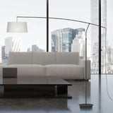 Raisa Fabric Drum Arc Floor Lamp in matt black, with a slim iron stem and curved overarching arm holding a white fabric drum shade, shown beside a sofa in a city-view living room.