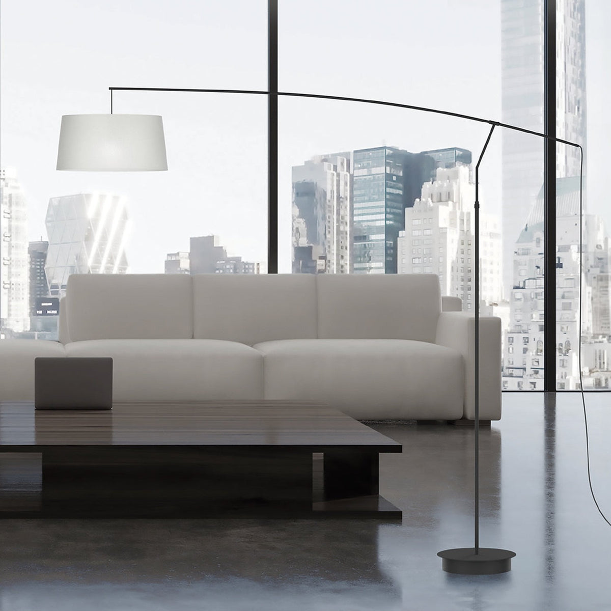 Raisa Fabric Drum Arc Floor Lamp in matt black with a slim iron stem and curved arm, white fabric drum shade, shown beside a sofa in a living room setting.