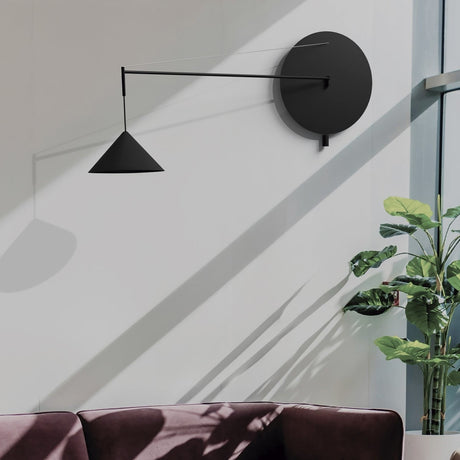 Roma Cone Wall Light in matt black, with round disc backplate, slim extending arm, wire support, and conical shade, shown mounted in a living room setting.