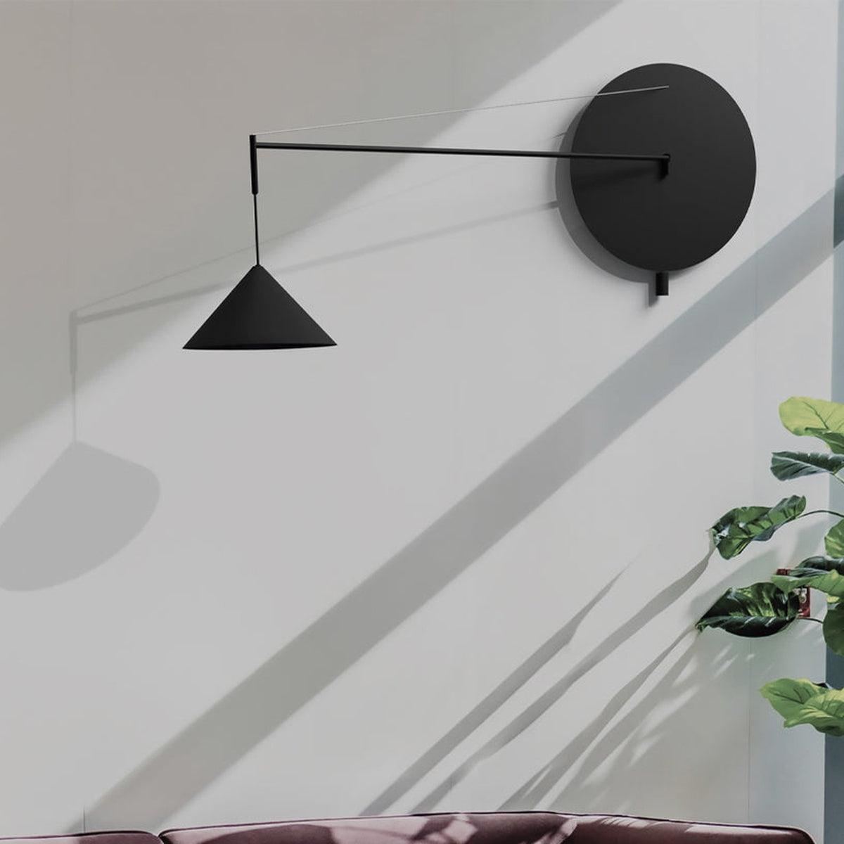 Roma Cone Wall Light in matt black with opal glass, extending from a round backplate on a long slim arm with wire support to a conical shade, shown on a grey wall beside a potted plant.