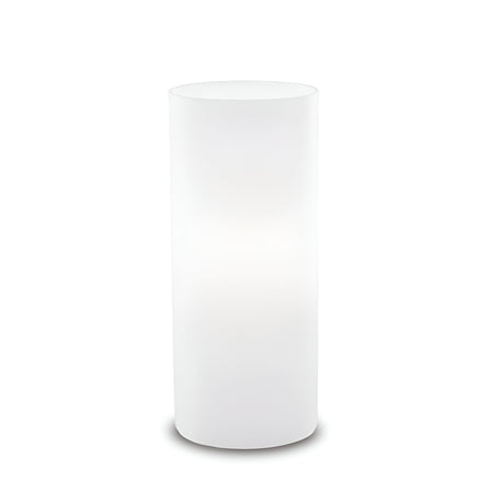 The Lumira Small Table Lamp - White, with its compact design and cylindrical form, is equipped with a blown white glass diffuser. When illuminated against a simple backdrop, it casts a gentle, warm glow through its opaque surface, elevating the minimalist and contemporary style.