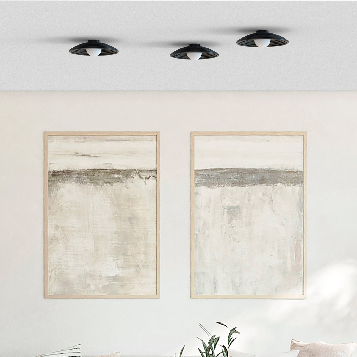 Three Randa flush ceiling lights in matt black with ribbed dishes and opal glass globes, mounted above framed abstract art in a neutral living room.