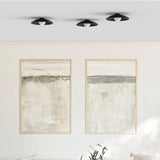 Three Randa flush ceiling lights in matt black with ribbed dishes and opal glass globes, mounted above framed abstract art in a neutral living room.