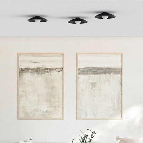 Three Randa flush ceiling lights in matt black with ribbed dishes and opal glass globes, mounted above framed abstract art in a neutral living room.