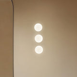 Rina Opal Glass Recessed Wall Light in polished brass, shown as three softly glowing round globes mounted vertically on a plain wall.