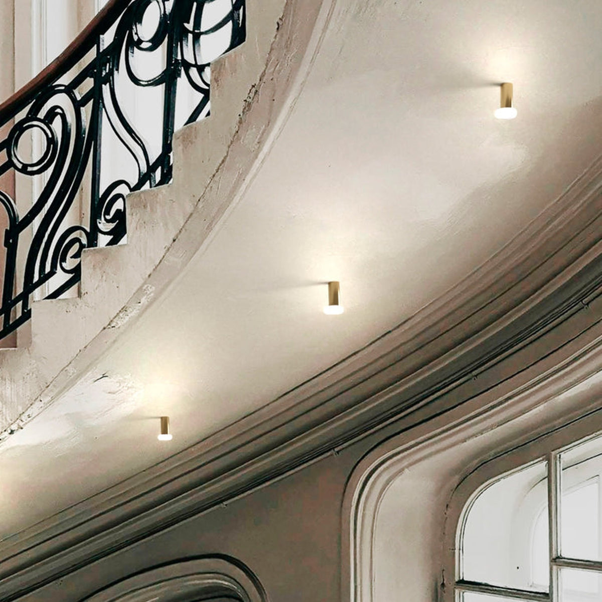 Rina Opal Glass Recessed Wall & Ceiling Light in polished brass, shown installed along a curved stairwell ceiling with multiple units casting a soft ambient glow.