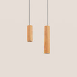 Taria Cylinder Pendant Light in Ash shown in two heights, slim wood cylinder shades on black textile cables against a plain light background.