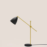 Nala Dome Adjustable Table Lamp with matt black dome shade on a long gold counterbalanced arm, pivoting on a slim gold upright with round marble base, shown against a plain light background.