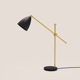 Nala Dome Adjustable Table Lamp with matt black dome shade on a long gold counterbalanced arm, pivoting on a slim gold upright with round black marble base, shown on a plain light background.