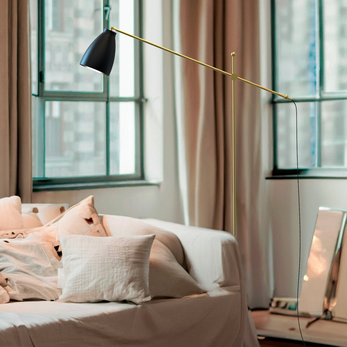 Nala Adjustable Floor Lamp with Marble Base in Matt Black & Gold, shown bedside with its angled gold arm and black dome shade extending over a bed.